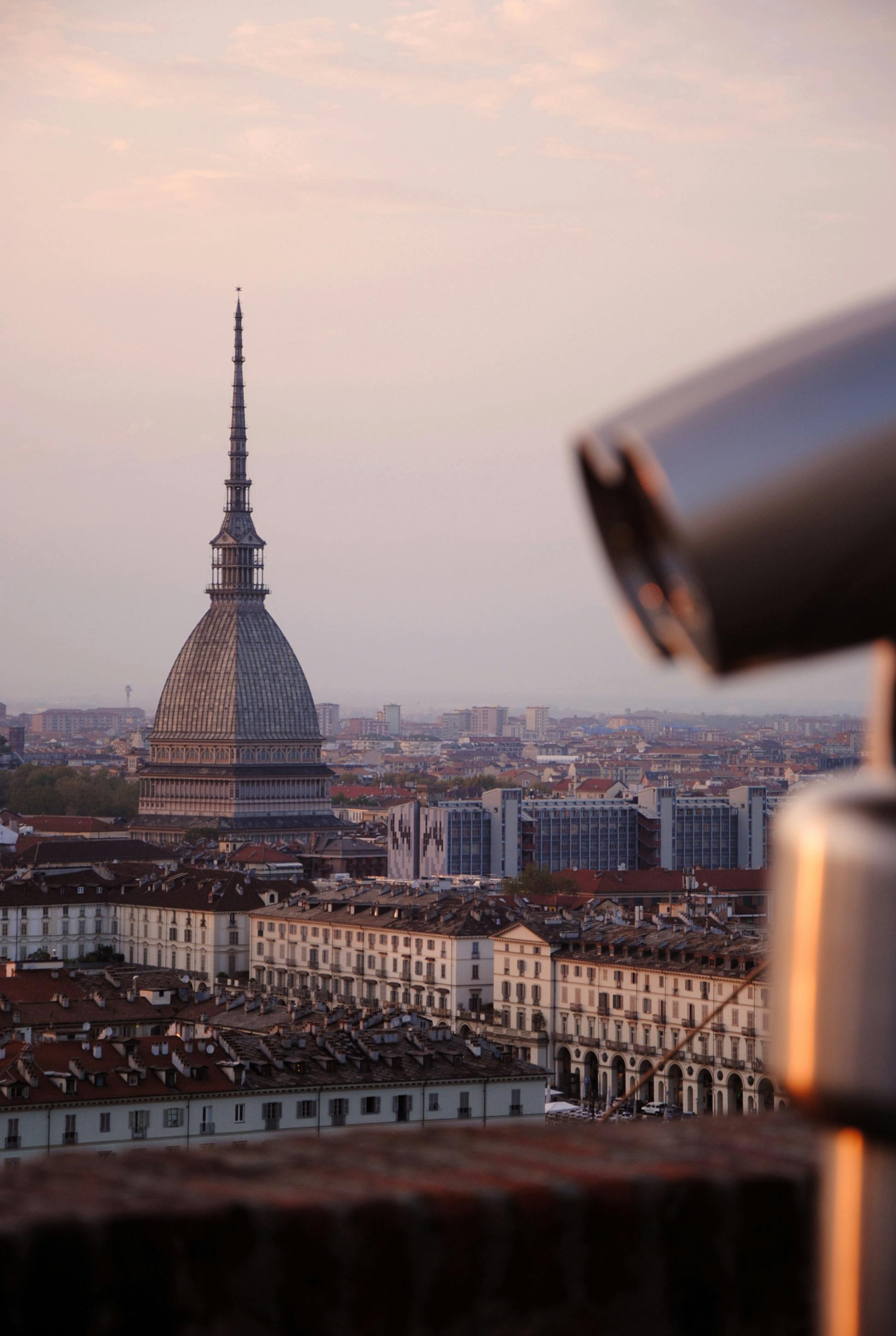 Captivating view of Turin's skyline featuring the Mole Antonelliana at sunset with a telescope in the foreground.