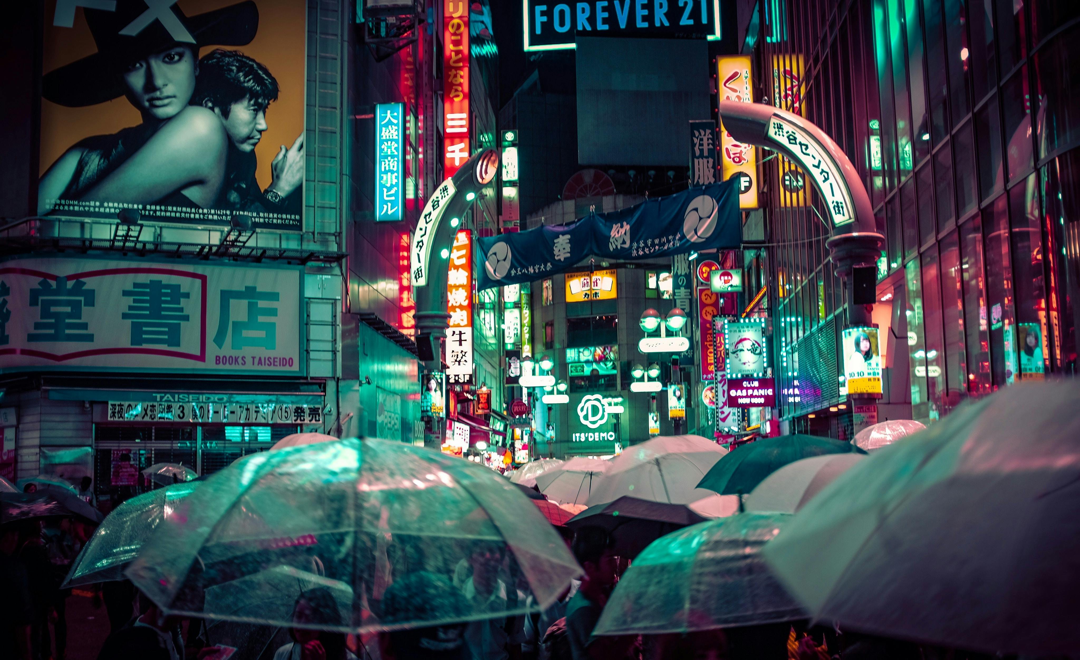 Explore Shibuya's bustling nighttime streets with neon lights and umbrellas amidst the rain in Tokyo, Japan.