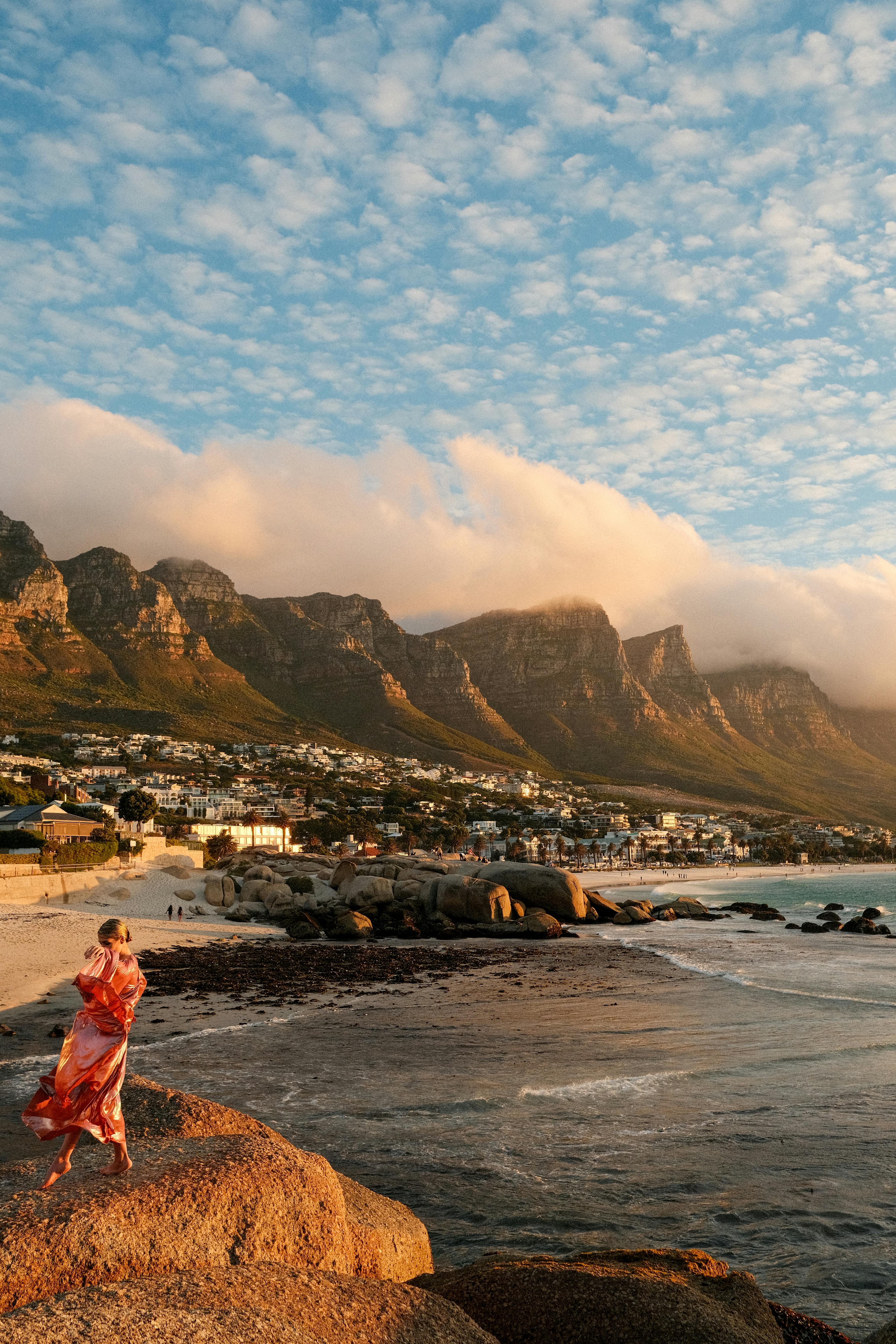 A scenic view of Cape Town's Twelve Apostles at sunset with a person in colorful attire.