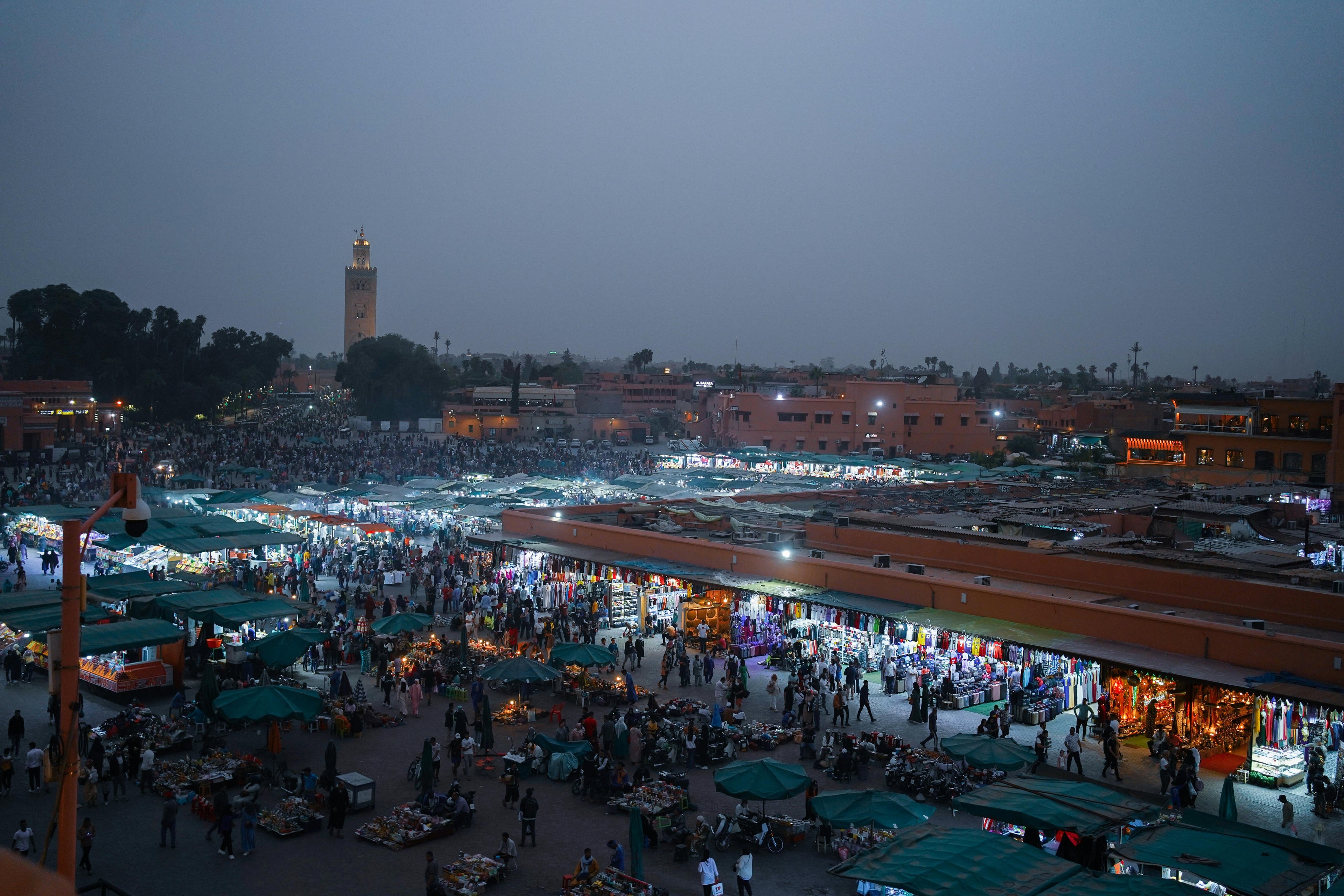 Aerial view of lively evening marketplace in Marrakech, filled with people and vibrant stalls.