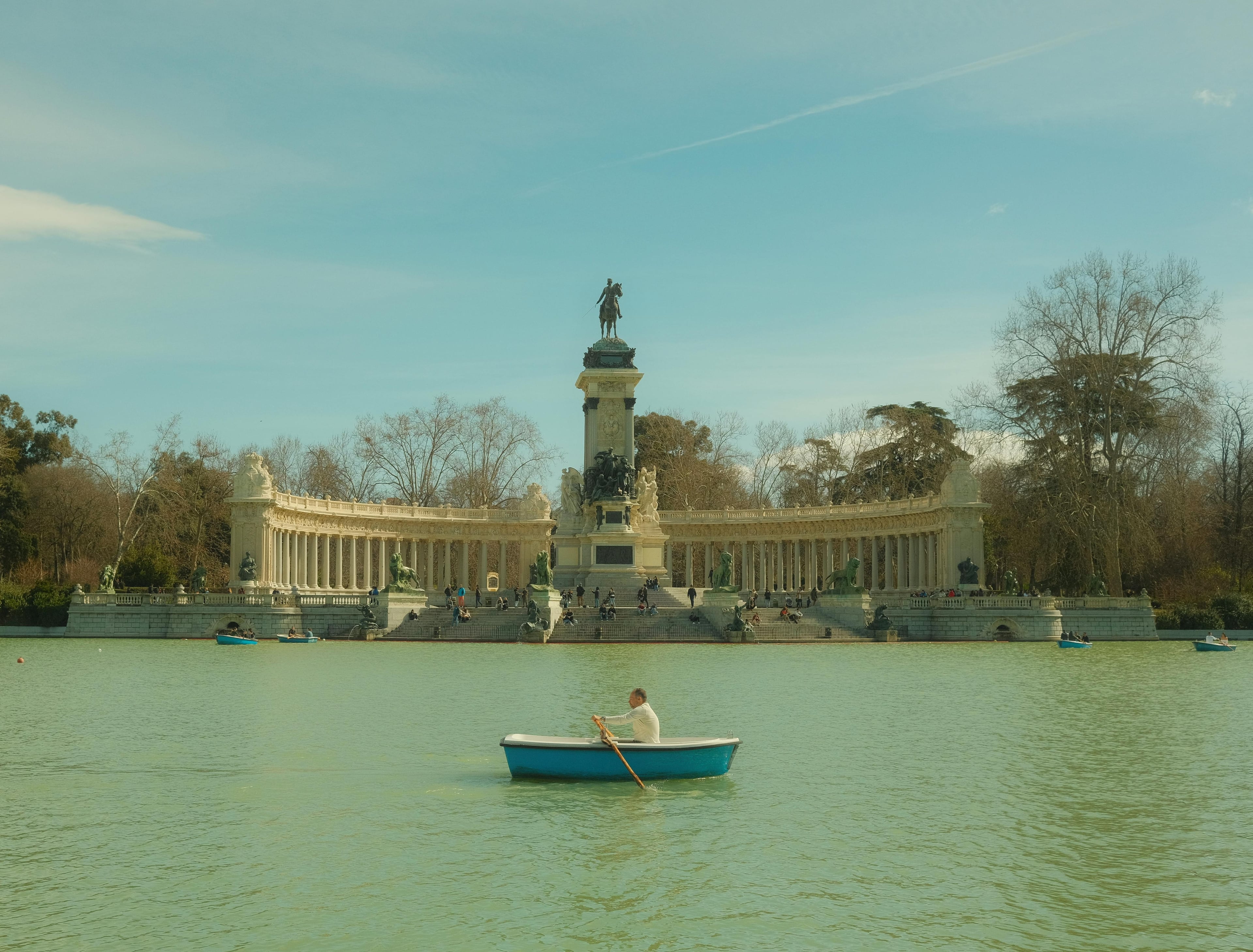 A serene view of a man rowing a boat at El Retiro Park with the Monument to Alfonso XII in Madrid.