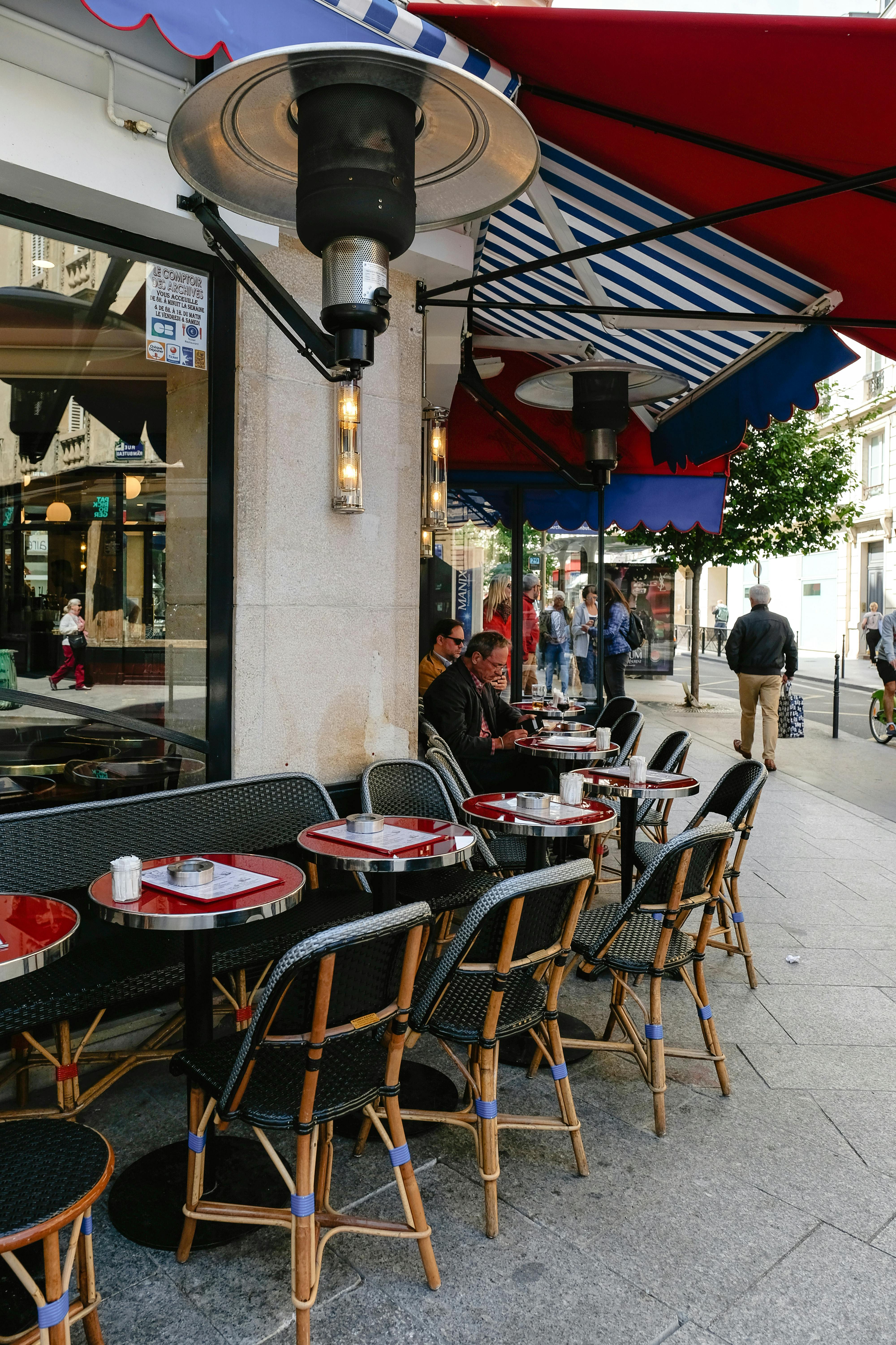 Charming Parisian café setting with outdoor seating and vibrant red awnings, capturing city life.
