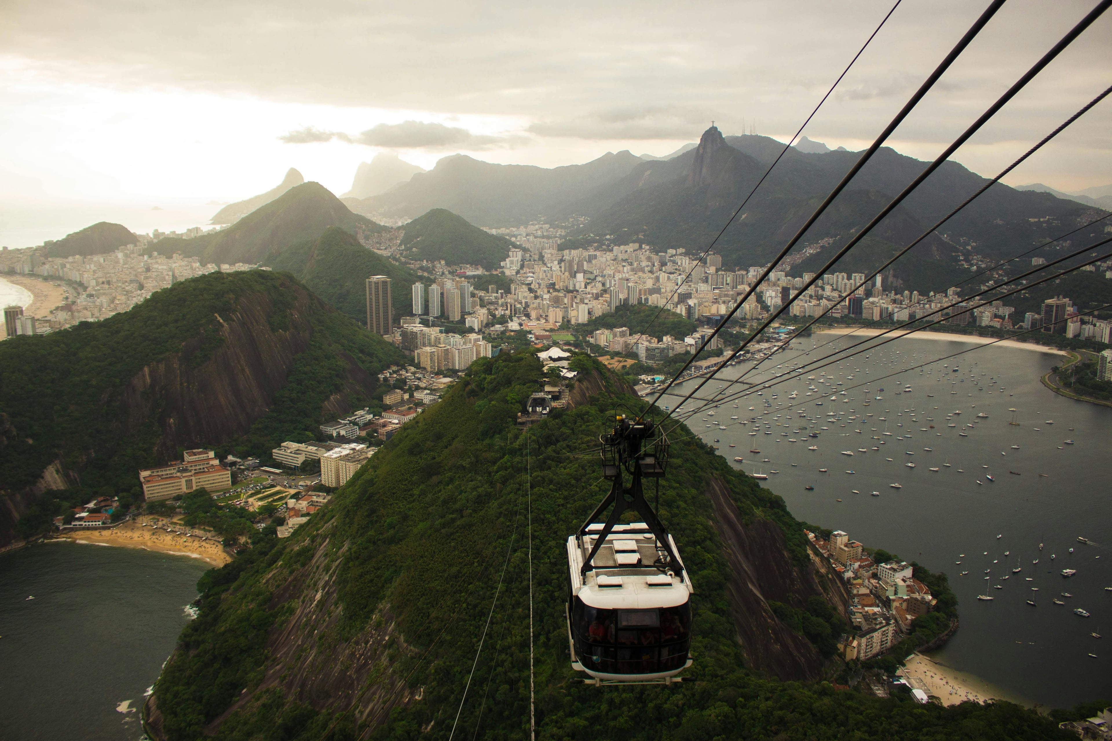 An aerial view of Rio de Janeiro's skyline with a cable car descending from Sugarloaf Mountain at sunset.