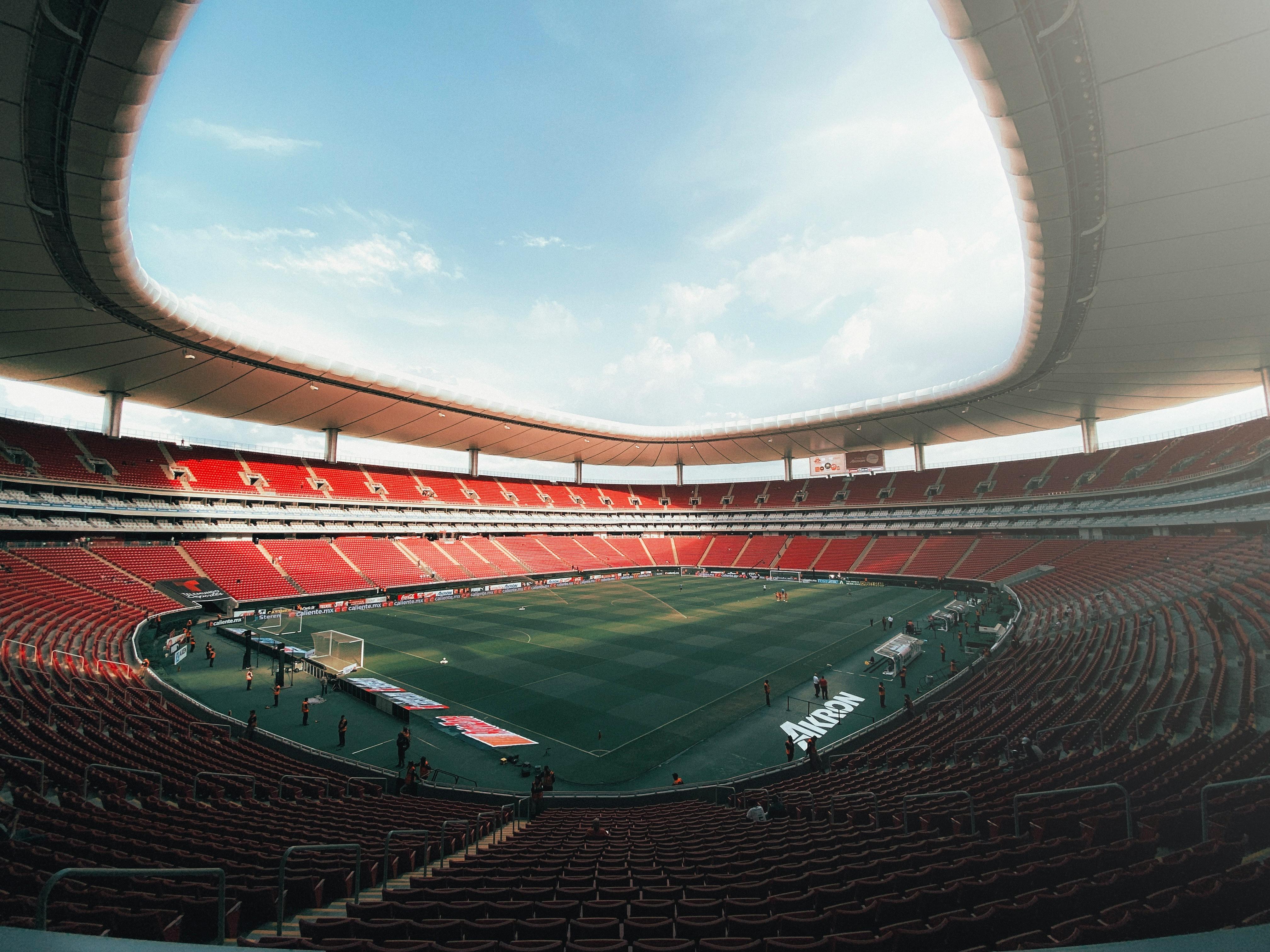 Aerial view of Estadio Akron in Guadalajara, Mexico, showcasing its vast red seating area and green soccer field.