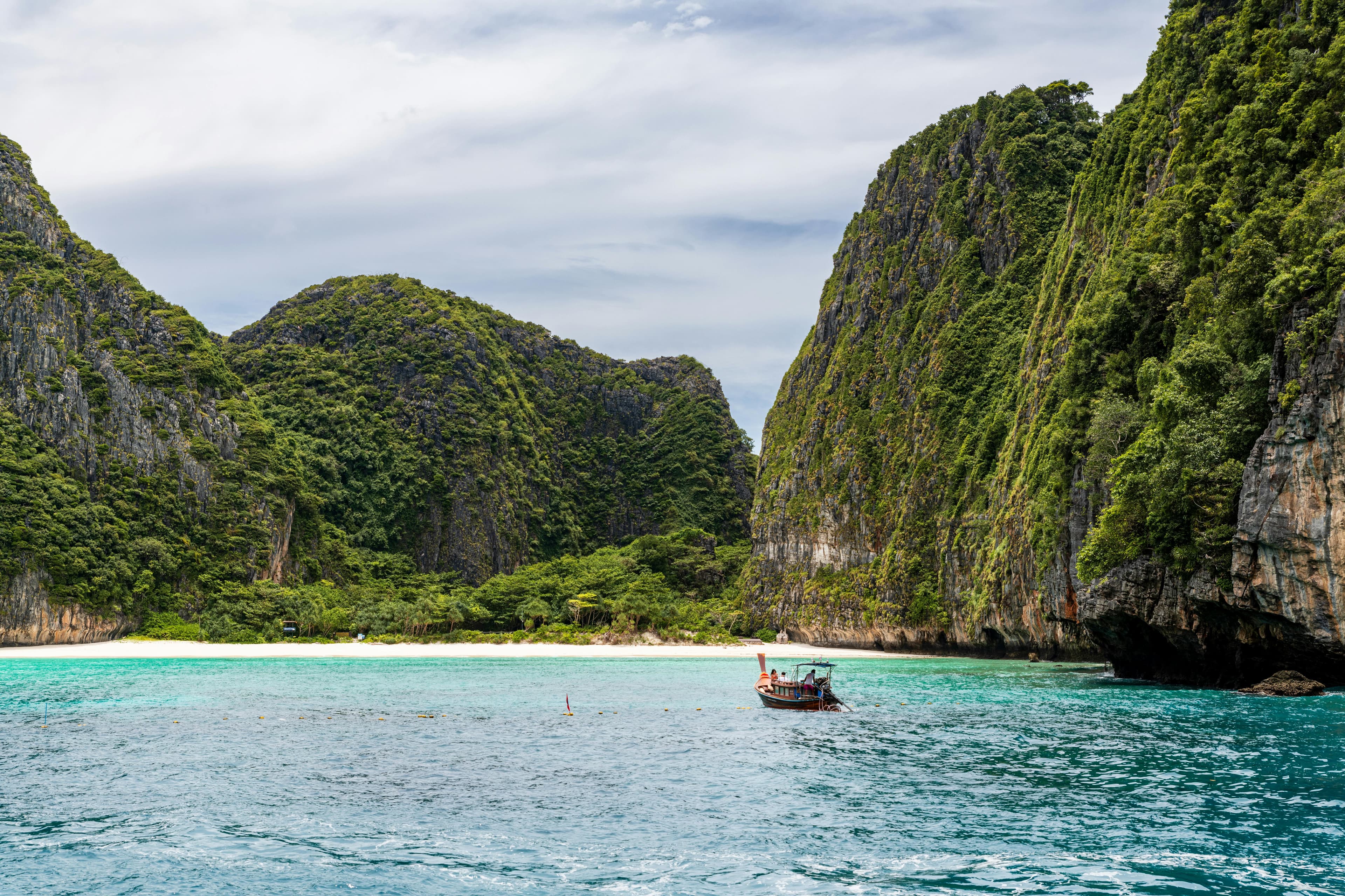 Idyllic view of a traditional boat against limestone cliffs and turquoise waters in Phuket, Thailand.